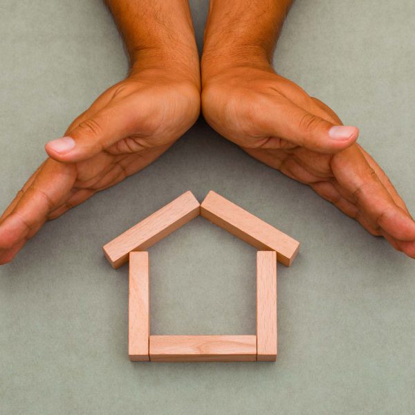 Mortgage concept on greenish grey background flat lay. hands enc Mortgage concept on greenish grey background flat lay. hands enclosing wooden house.